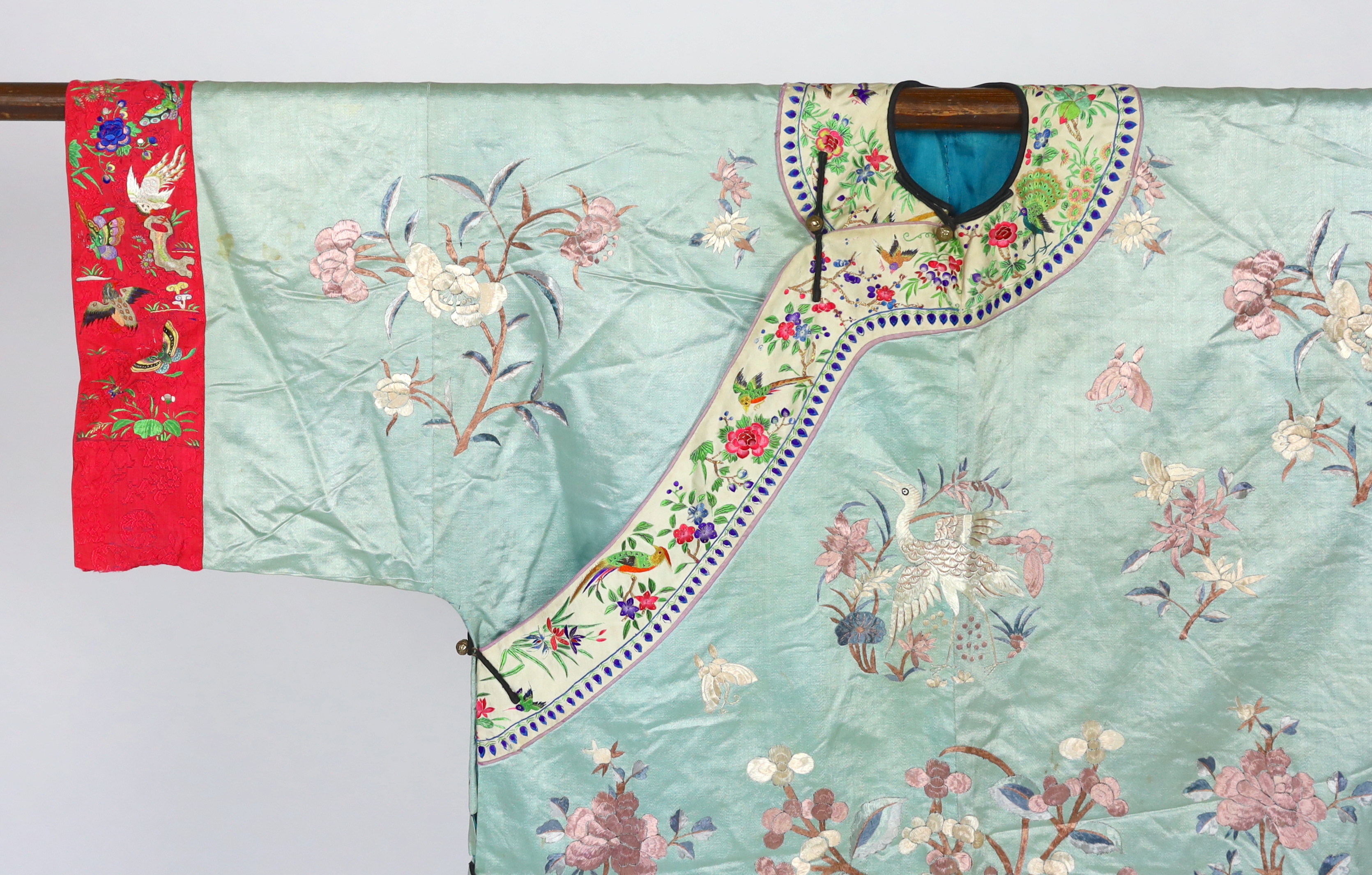 An early 20th century Chinese silk embroidered turquoise robe, embroidered in pastel silk with butterflies and flowers all over, polychrome embroidered braiding edged with lilac and bright pink sleeve bands embroidered w